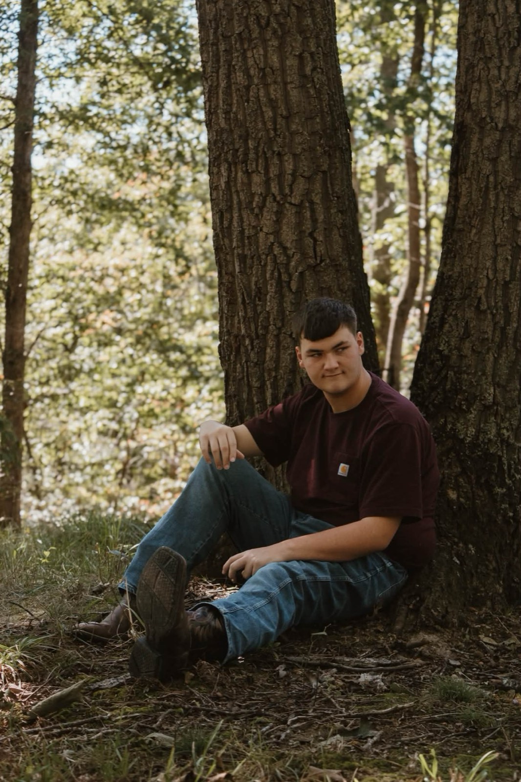 Dylan Kouns, class of 2027, seated against a tree in a senior portrait by Omens Photography.
