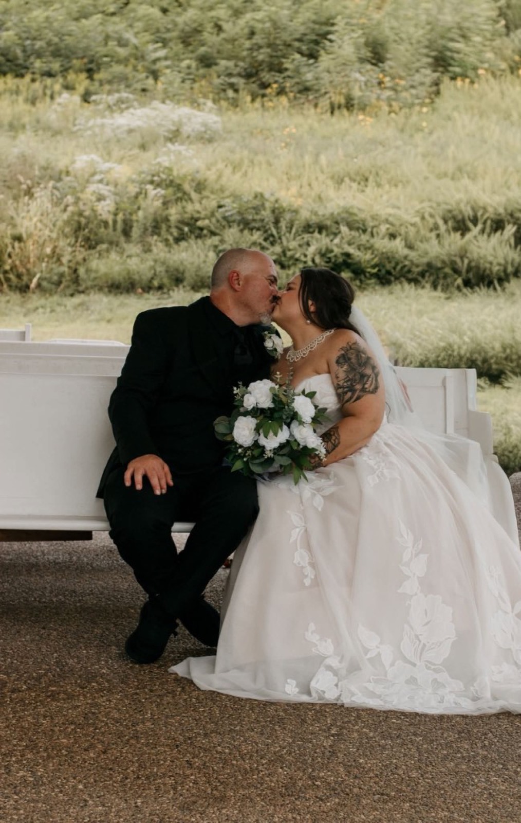A bride and groom kissing on a white bench, photographed by Omens Photography.